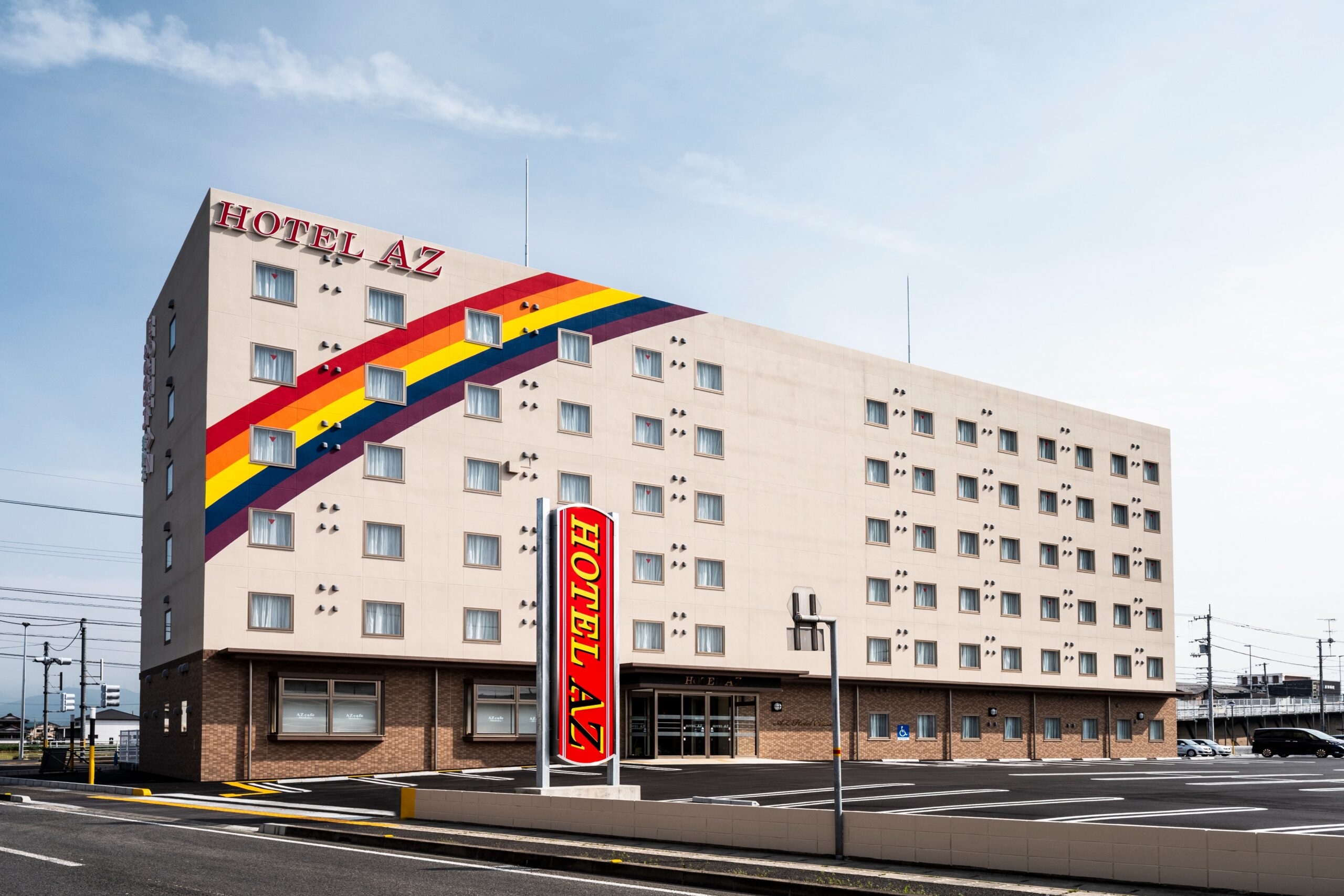 HOTEL AZ 岡山備前店の公式サイトに掲載された外観写真 — 白い外壁に虹色のラインと縦型の看板