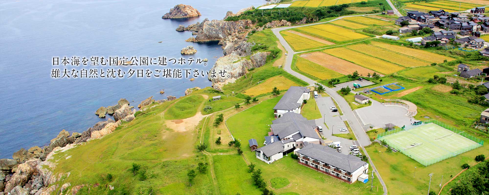 ホテルファミリーオ佐渡相川 — 新潟県佐渡市小川 · 日本海沿いの台地に建つ全30室のホテルとテニスコートの空撮