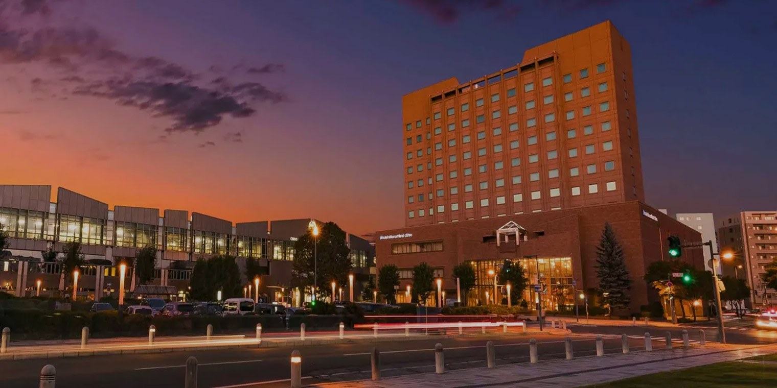 ホテル日航ノースランド帯広 — 帯広市西2条南・JR帯広駅隣接 · 夕暮れの外観と左手の帯広駅舎