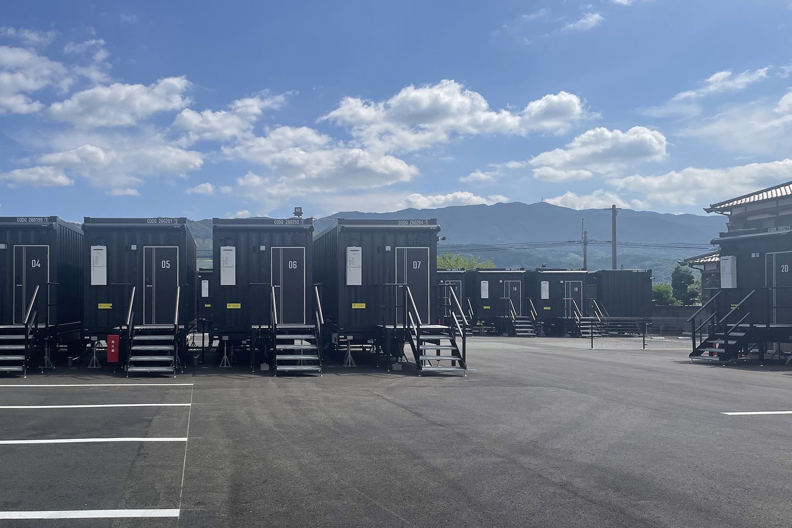 HOTEL R9 The Yard うきは — 福岡県うきは市吉井町 · 平面駐車場に沿って並ぶ1台1室のコンテナ客室